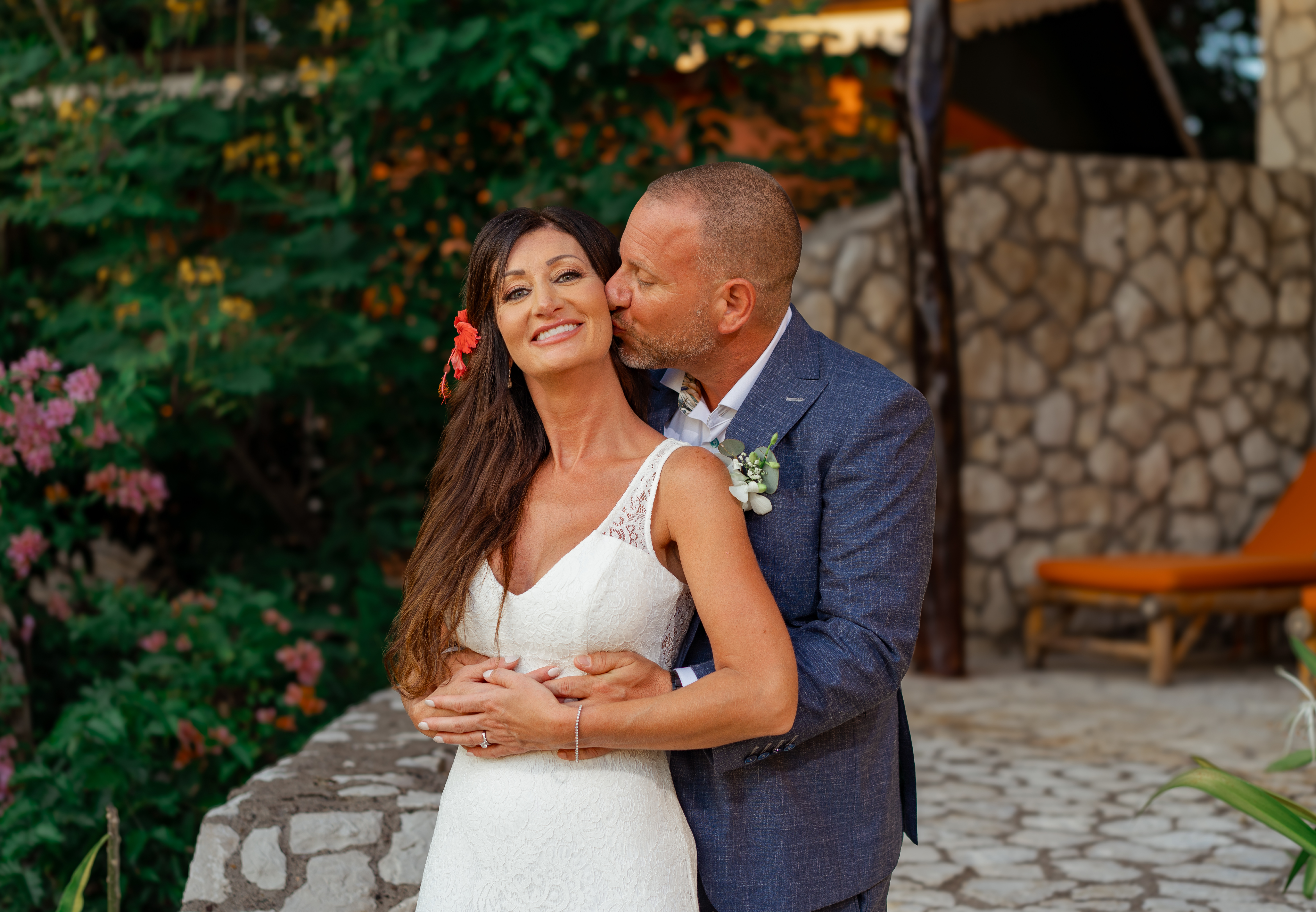 Joe kissing Sarah on the cheek in the tropical garden, she is beaming