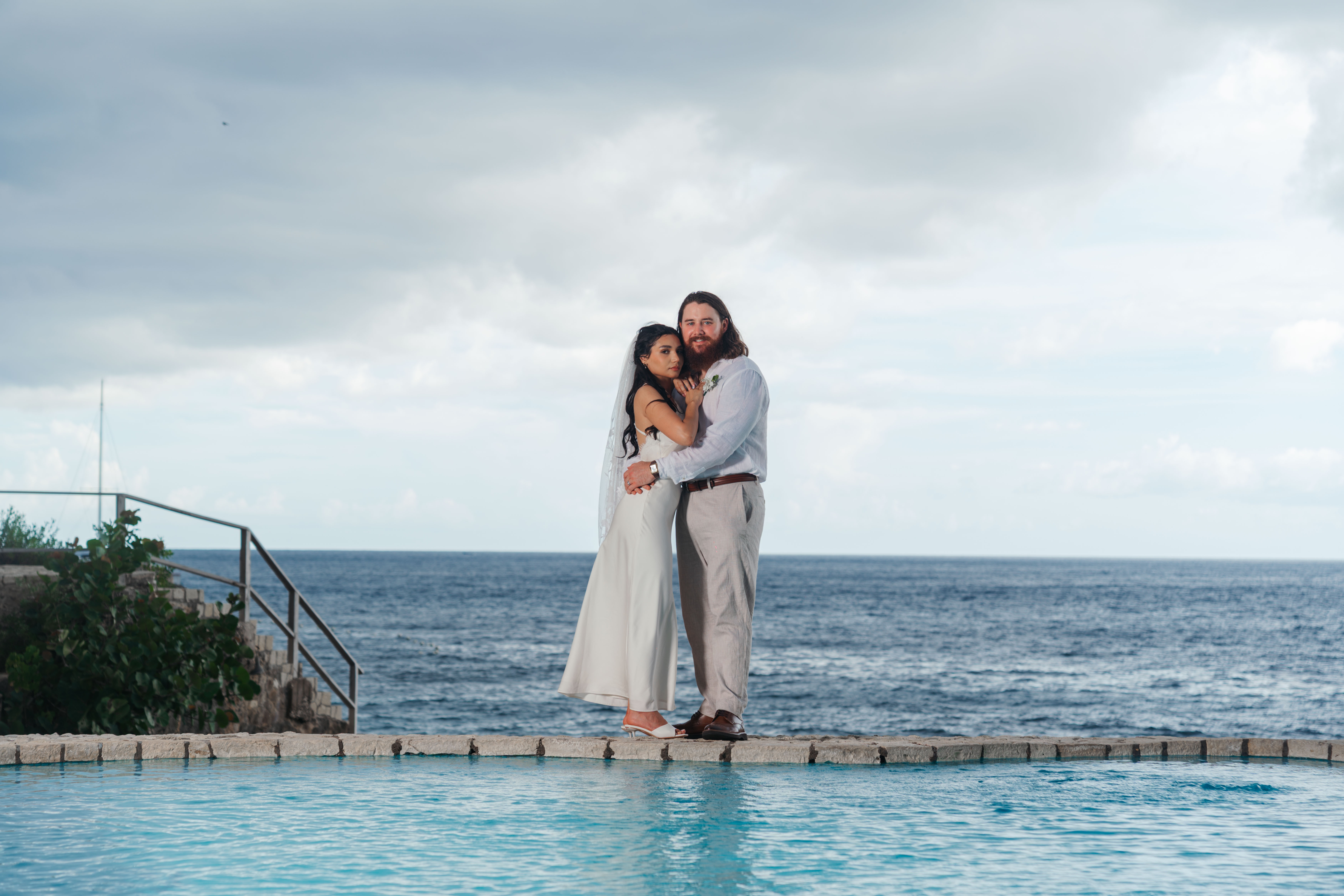 Couple embracing by the cliffside pool, ocean behind